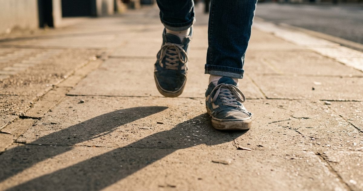 Unos pies con zapatillas caminando por la acera, con la sombra larga de la tarde